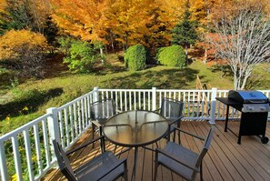 A deck with a round glass table and four chairs, a barbecue grill, and a white railing.