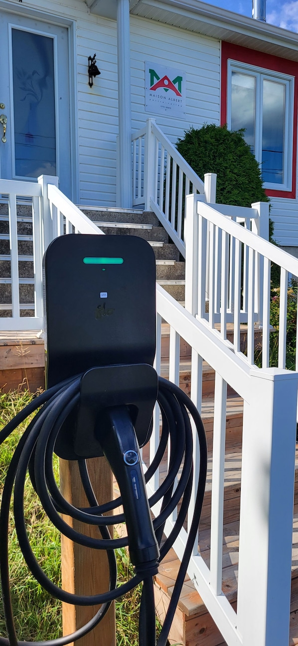 An electric vehicle charging station in front of a house with a white fence and a mailbox.