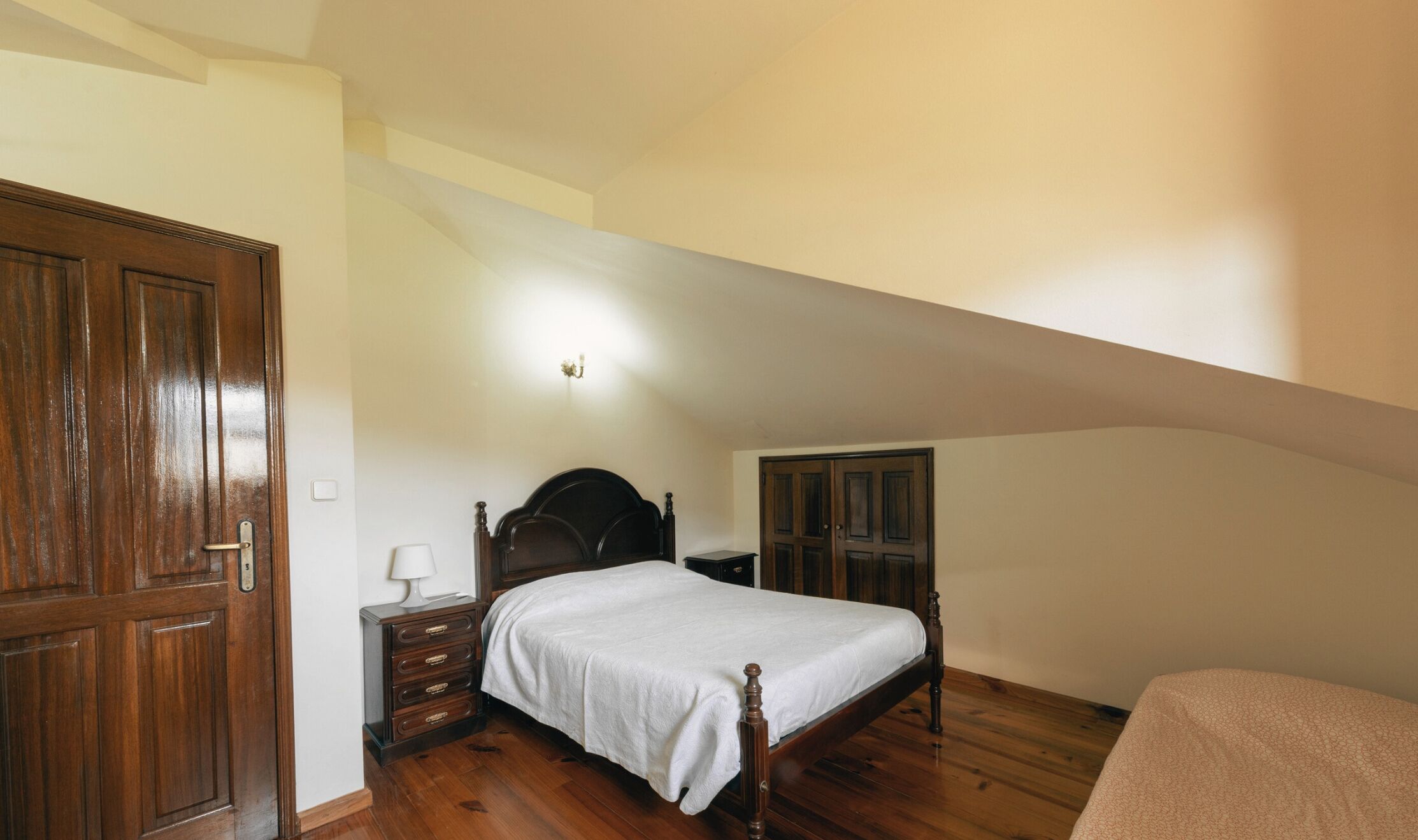 Un dormitorio con una cama de madera, una mesita de noche, un aparador y una puerta.