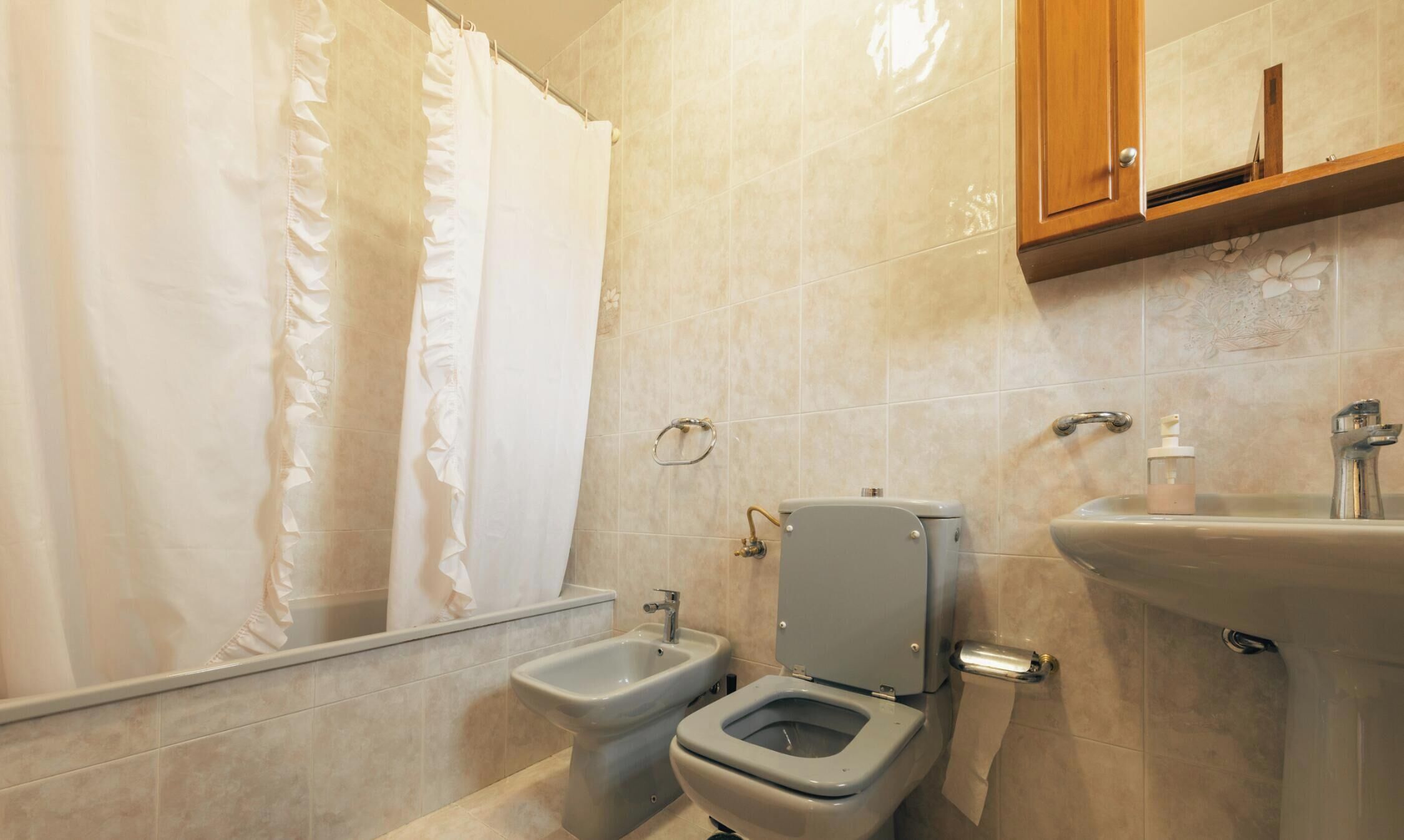 A bathroom with a toilet, bidet, sink, and a shower curtain.