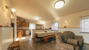 A spacious living area with a dining table, two sofas, a kitchen with wooden cabinets, and a large window. - Casa da Pedra by ALPONTE (Venade)