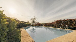 A swimming pool surrounded by greenery and a house in the background. - Casa da Pedra by ALPONTE (Venade)