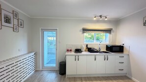 A modern kitchen with white cabinets, a microwave, and a window above the sink. - Hot Spring Vacation House (Rotorua)
