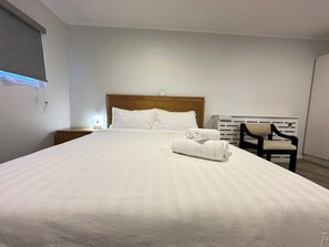 A hotel room with a large bed, a wooden headboard, a nightstand with a lamp, a chair, and a radiator. - Hot Spring Vacation House (Rotorua)