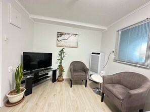 A living room with a flat-screen TV, a potted plant, a gray armchair, a round table, and a standing heater.