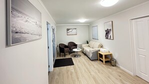 A hallway with a wooden floor, a sofa, a chair, a small table, and a picture of a koala on the wall. - Hot Spring Vacation House (Rotorua)
