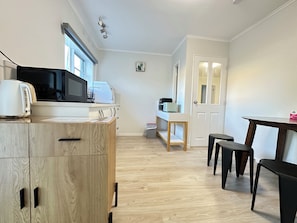 A compact kitchen with a microwave, toaster, and a small table with stools.
