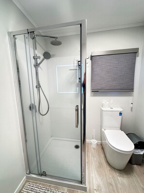 Ein modernes Badezimmer mit einer Duschkabine, einer Toilette und einem Fenster mit Jalousie.