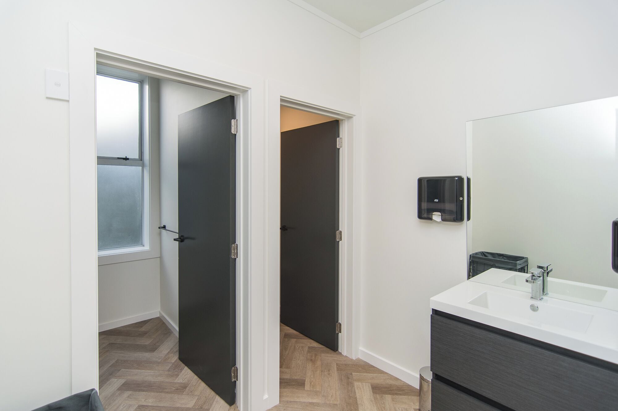 A modern bathroom with a white sink, dark cabinet, and a large mirror.