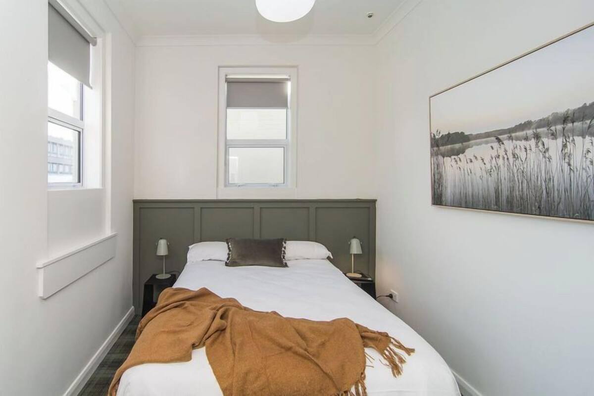 A bedroom with a bed, two bedside tables, a window, and a wall-mounted painting.