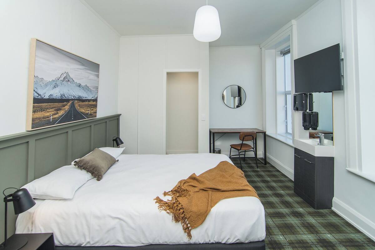 A hotel room with a bed, a desk, a chair, a mirror, and a window.