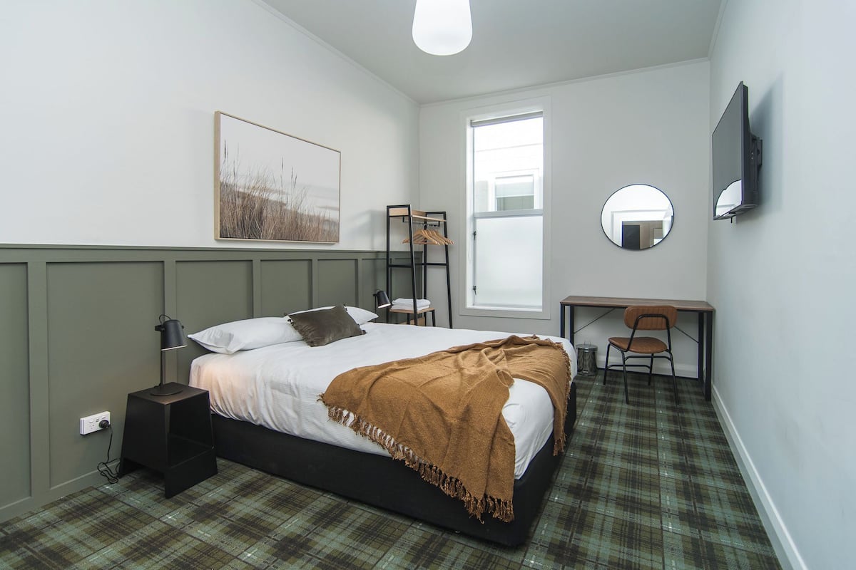 A bedroom with a bed, bedside table, lamp, and a desk with a chair.