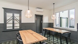 Un salón de conferencias con una mesa de madera y sillas negras, dos lámparas colgantes, una puerta y una ventana con vistas a un edificio.