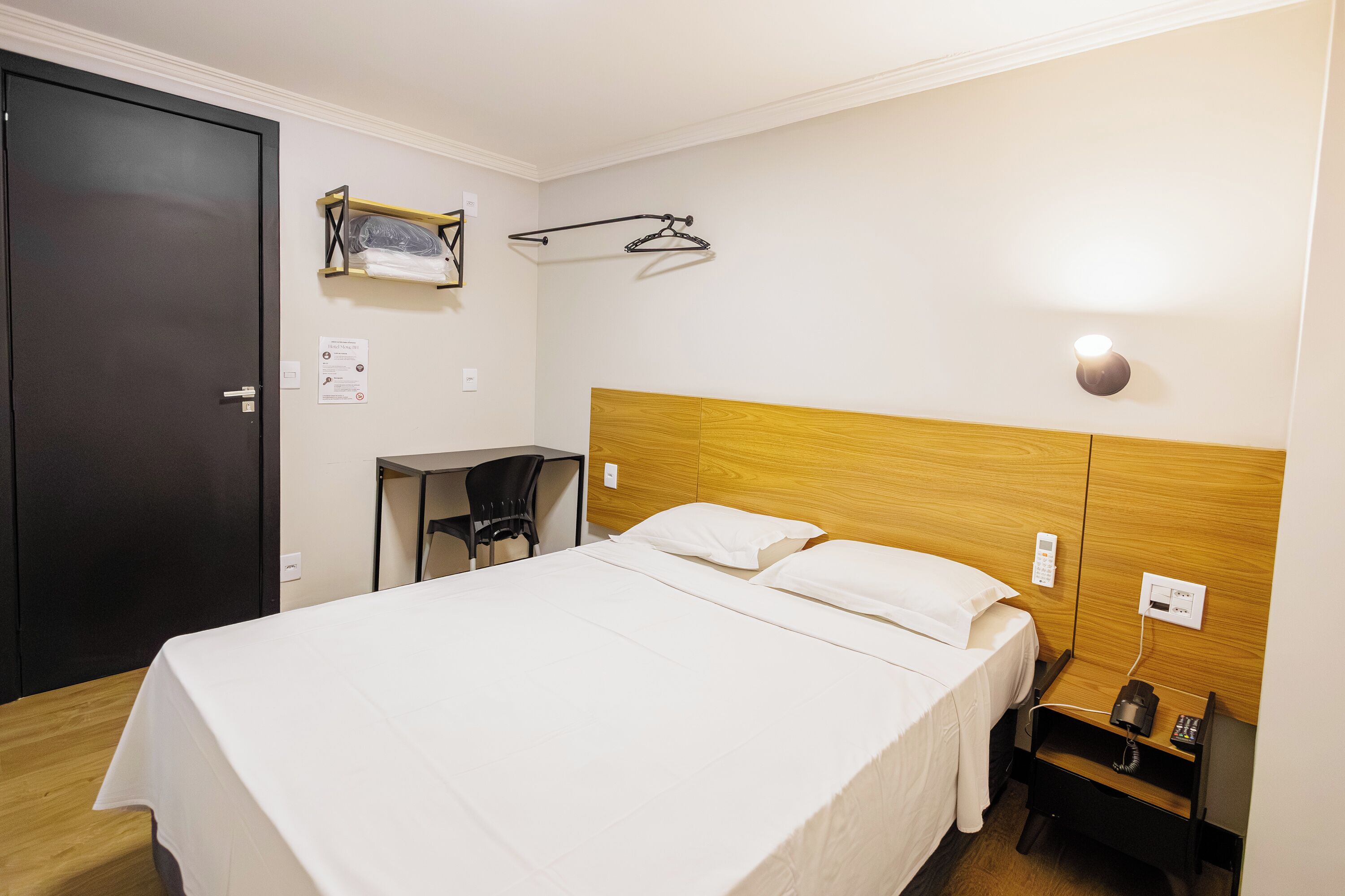 Hotellihuone, jossa on sänky, työpöytä, tuoli, naulakko ja yöpöytä, jossa on puhelin.