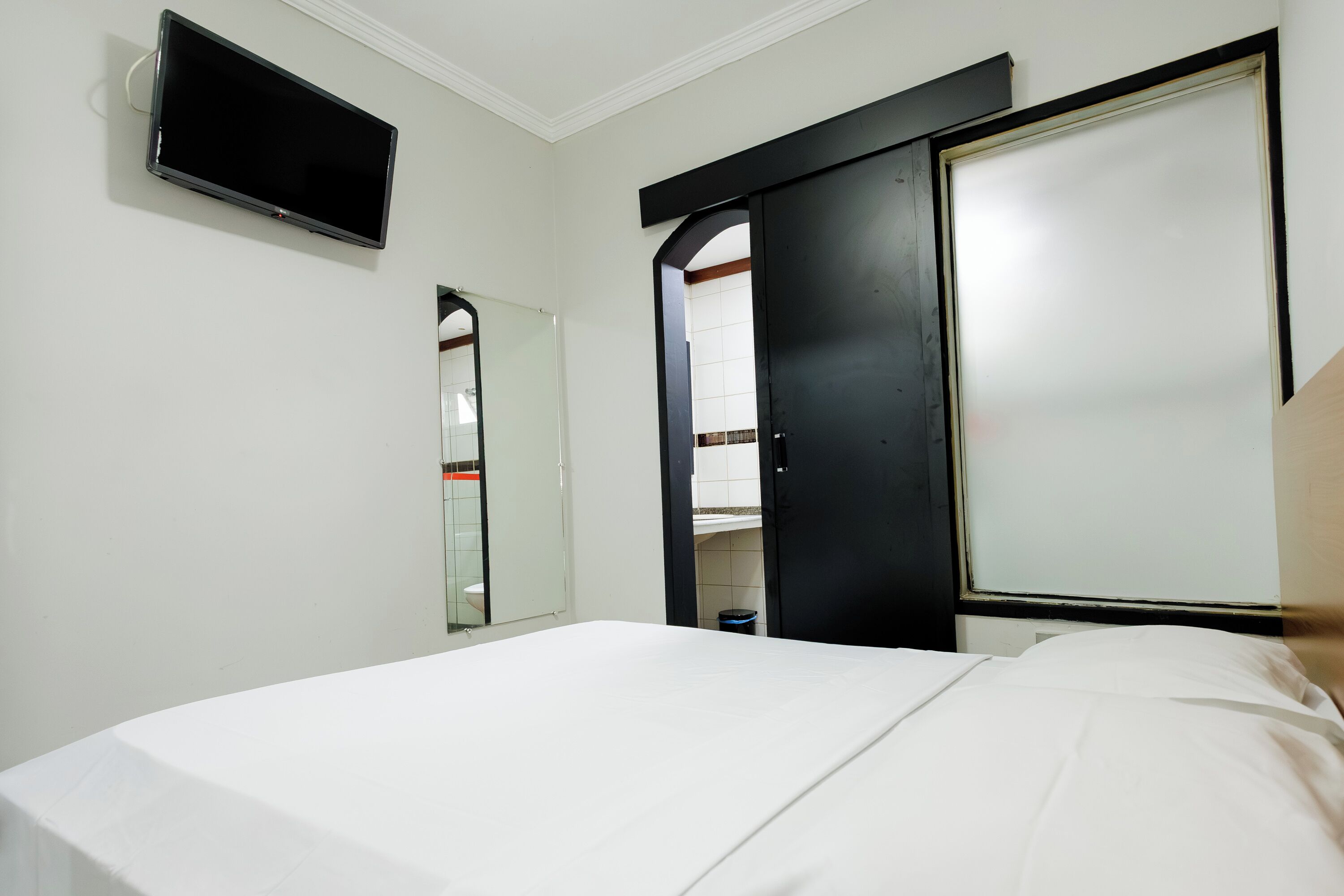 A hotel room with a bed, a flat-screen TV mounted on the wall, a mirror, and a wardrobe with a sliding door.