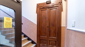 Une porte à double battant en bois, avec une enseigne au-dessus, un escalier avec des marches de couleur beige et un interrupteur sur le mur.