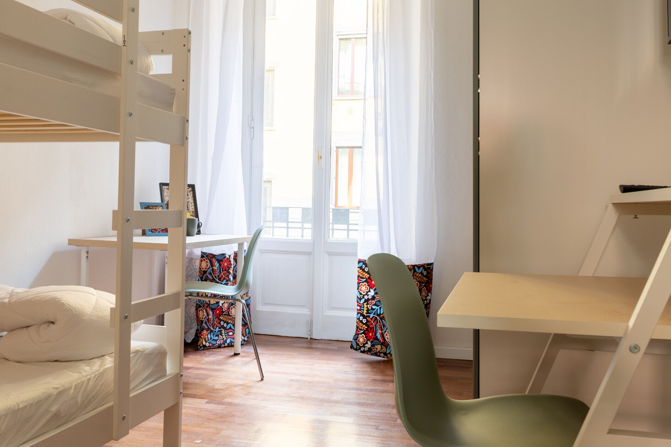 A room with a bunk bed, a desk, a chair, and a colorful curtain.