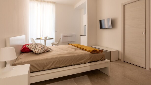 Et moderne hotelværelse med seng, sengebord, lampe, fjernsyn og et skrivebord med stol.