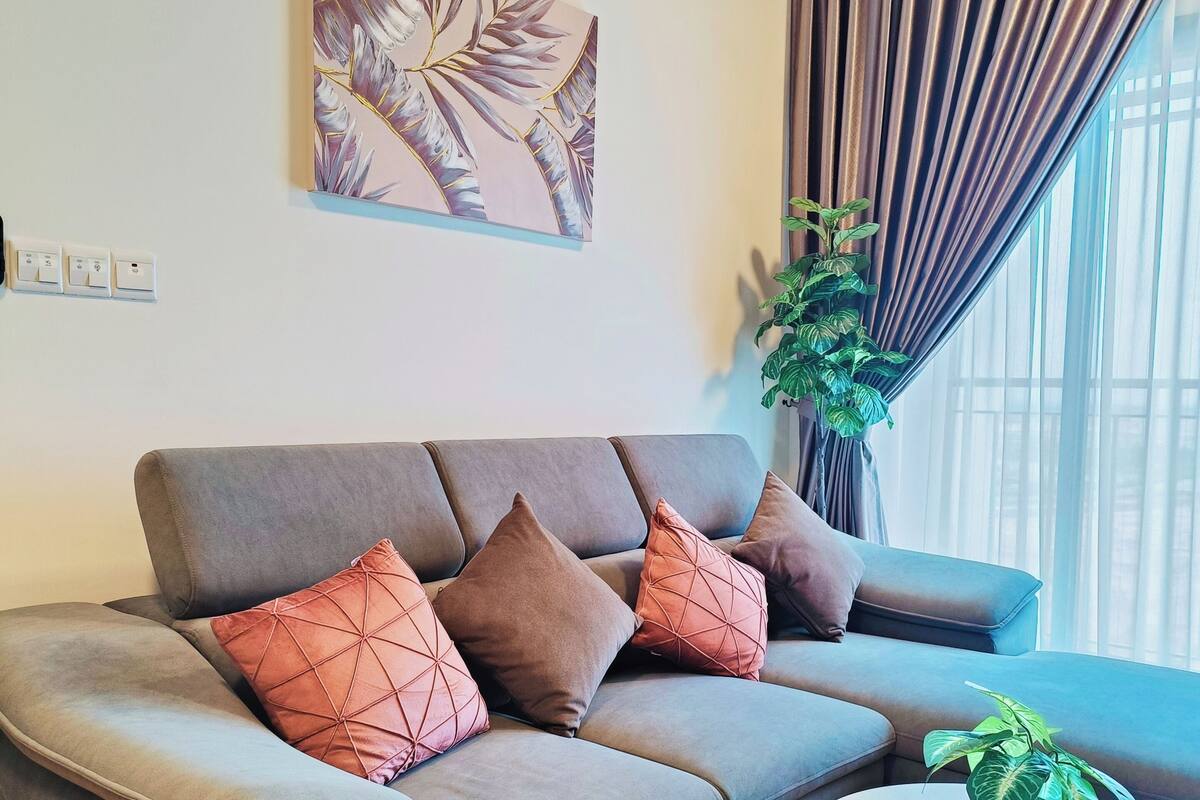 A modern living room with a grey sofa, geometric patterned cushions, a round coffee table, and a potted plant.