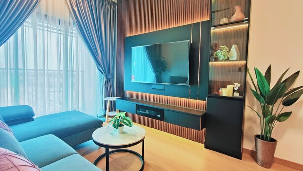 A modern living room with a large flat-screen TV, a sofa, a coffee table, and a potted plant. - MayaBay Residences Bandar Gamuda Cove (Banting)