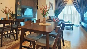 A modern living room with a dining area, featuring a wooden table and chairs, a flat-screen TV, and a ceiling fan. - MayaBay Residences Bandar Gamuda Cove (Banting)