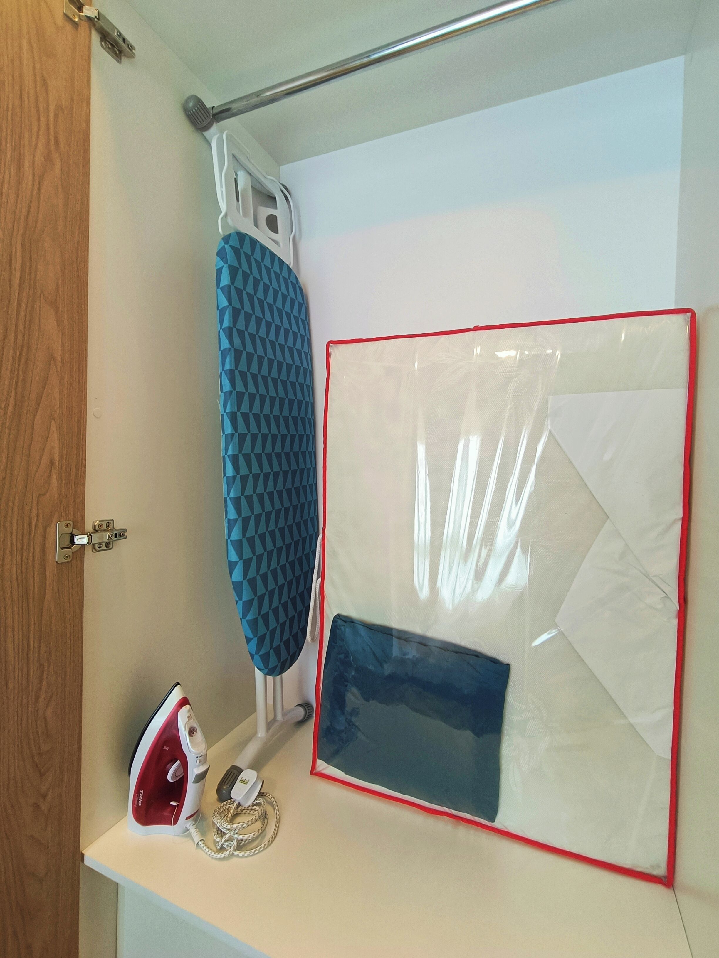 Een badkamer met een houten deur, een handdoekhouder, een douchekop en een witte plank met een strijkijzer en een opgevouwen handdoek.