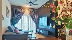 A modern living room with a wooden dining table, a sofa, a TV, and a ceiling fan. - MayaBay Residences Bandar Gamuda Cove (Banting)