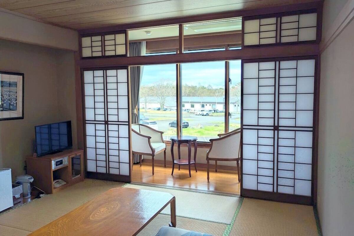 A traditional Japanese-style room with tatami flooring, a television, a small refrigerator, and a view of the outside.