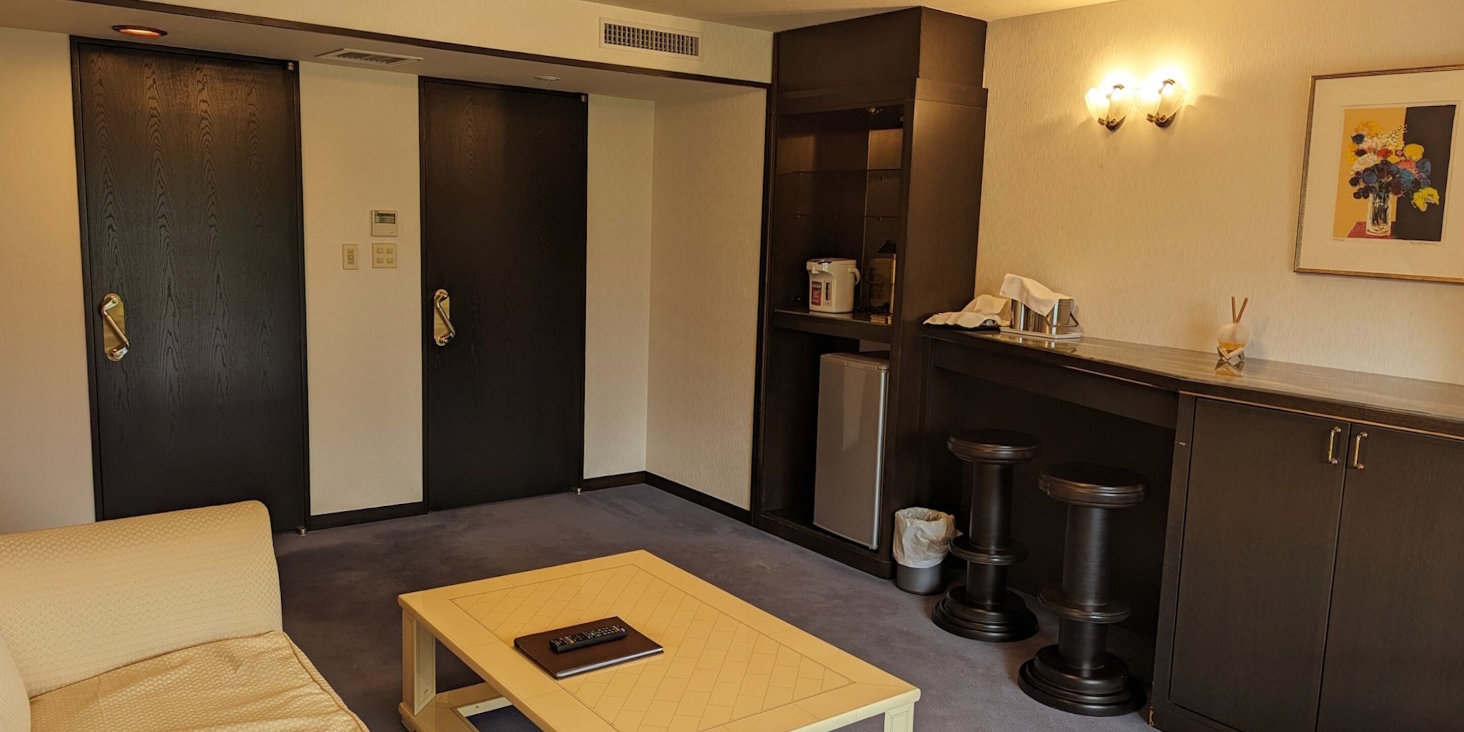A hotel room with a sofa, a small table, a minibar, and a door.