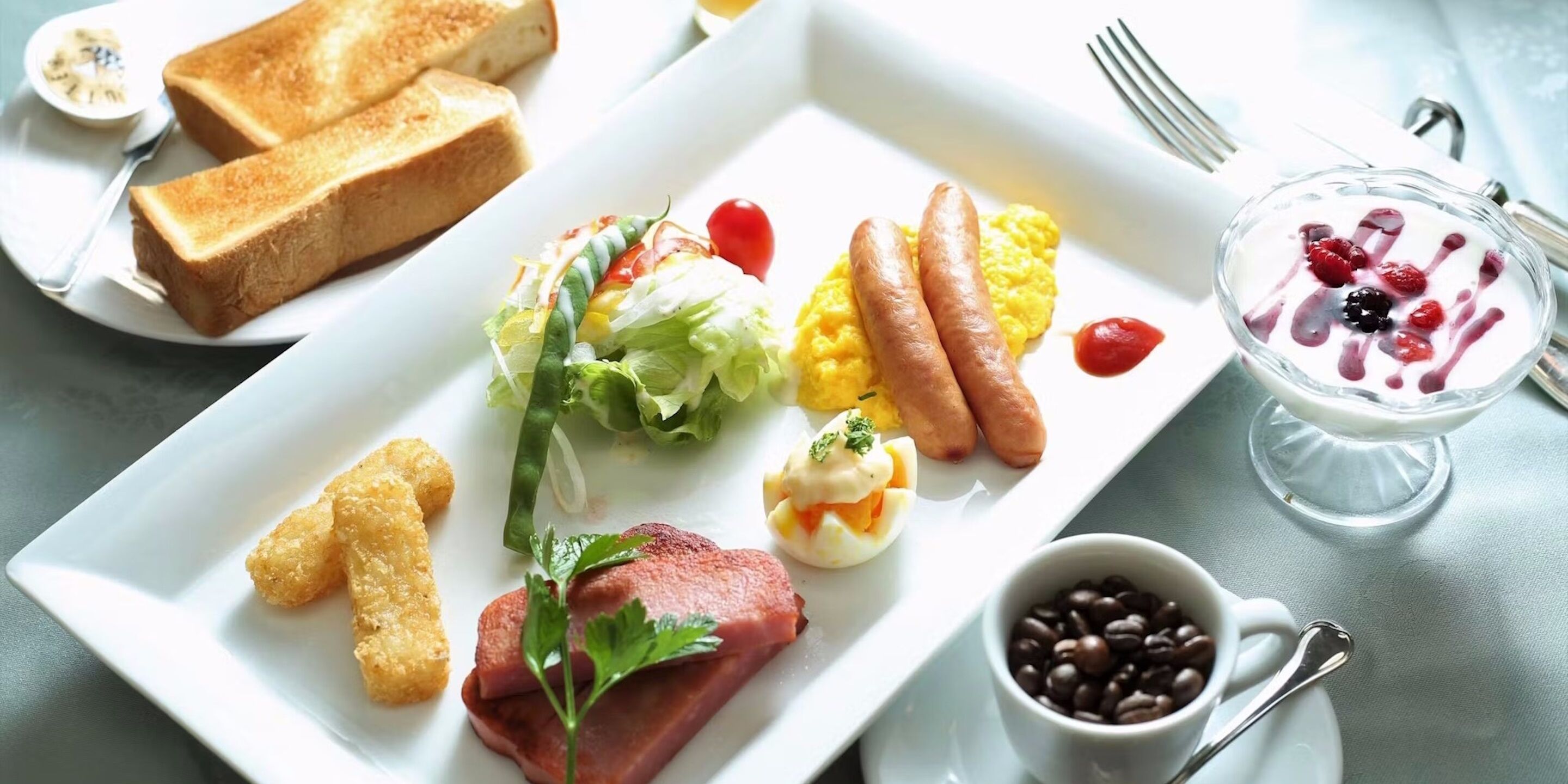 Ein Frühstücksteller mit Toast, Würstchen, Rührei, Salat und einer Kaffeetasse.