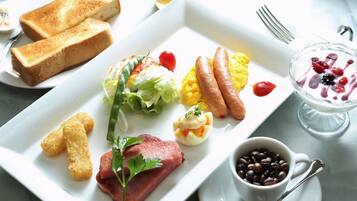 Ein Frühstücksteller mit Toast, Würstchen, Rührei, Salat und einer Kaffeetasse.