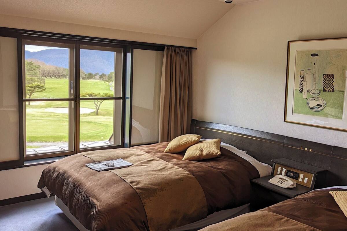 Une chambre d’hôtel avec deux lits, une grande fenêtre donnant sur un terrain de golf, un tableau encadré au mur et une table de chevet avec un téléphone et une lampe.