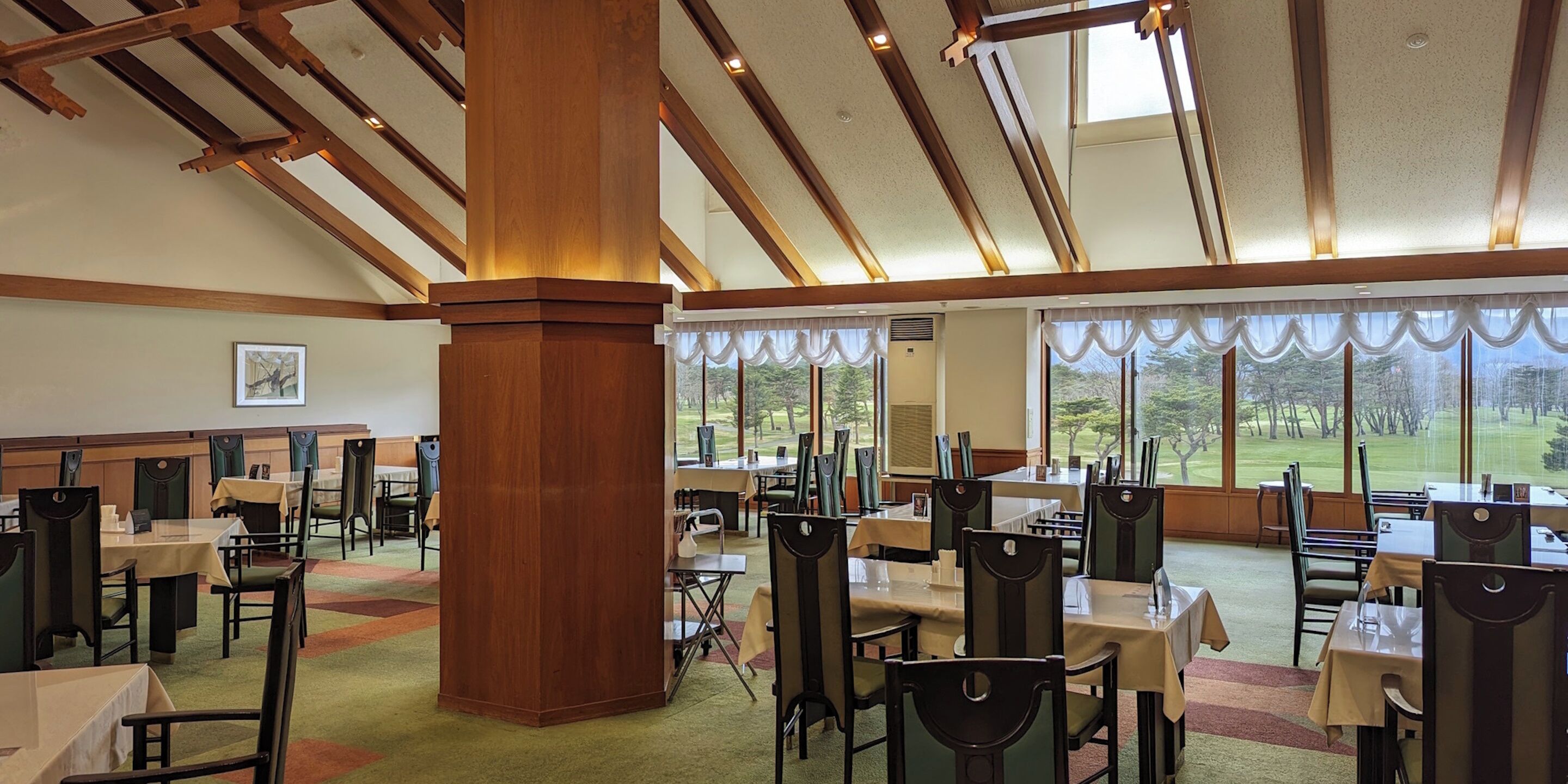 A spacious dining area with high ceilings, large windows, and a view of the outdoors.
