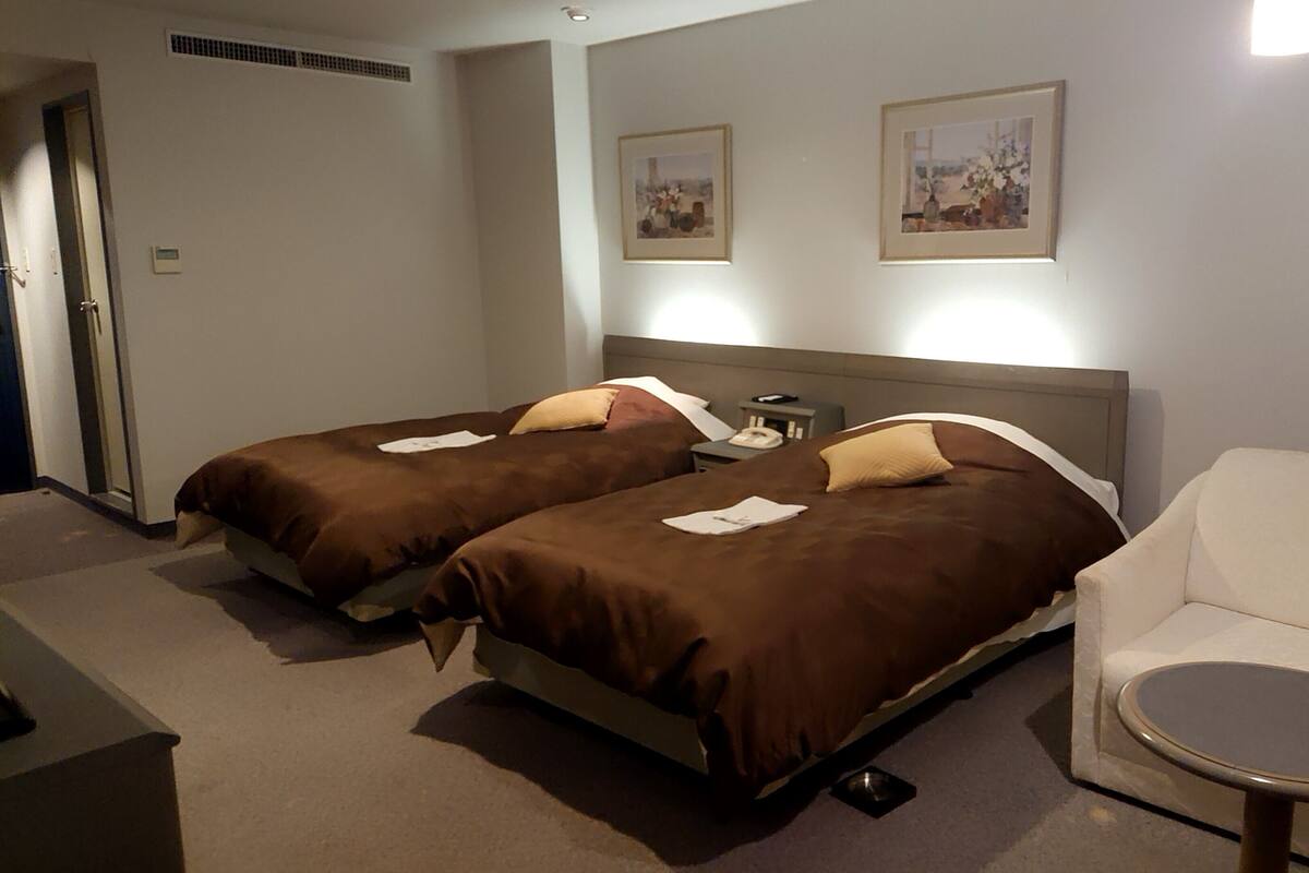 Une chambre d’hôtel avec deux lits, une petite table ronde, un canapé et deux tableaux encadrés au mur.