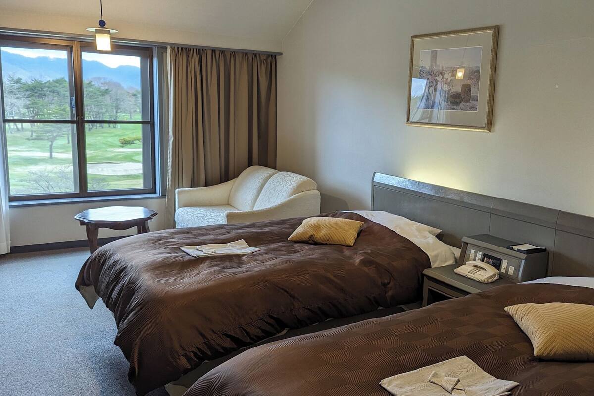 Une chambre d’hôtel avec deux lits, une chaise, une petite table et une table de chevet avec un téléphone.