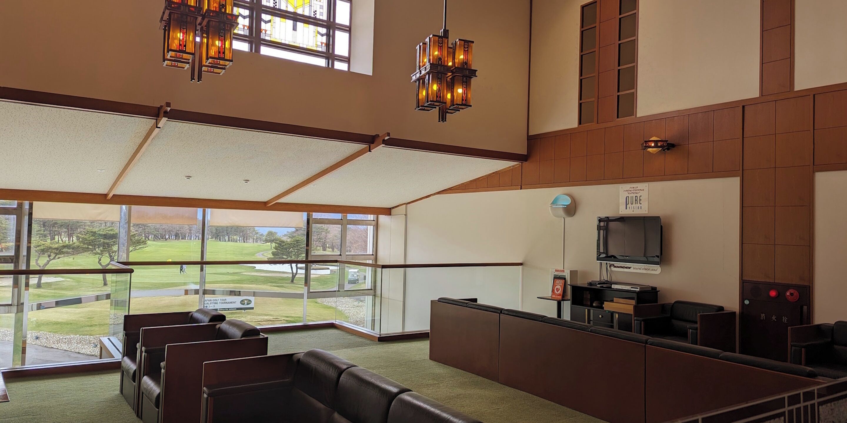 En rymlig lobby med utsikt över en golfbana, bekväma lädersitsar, en receptionsdisk och modern belysning.