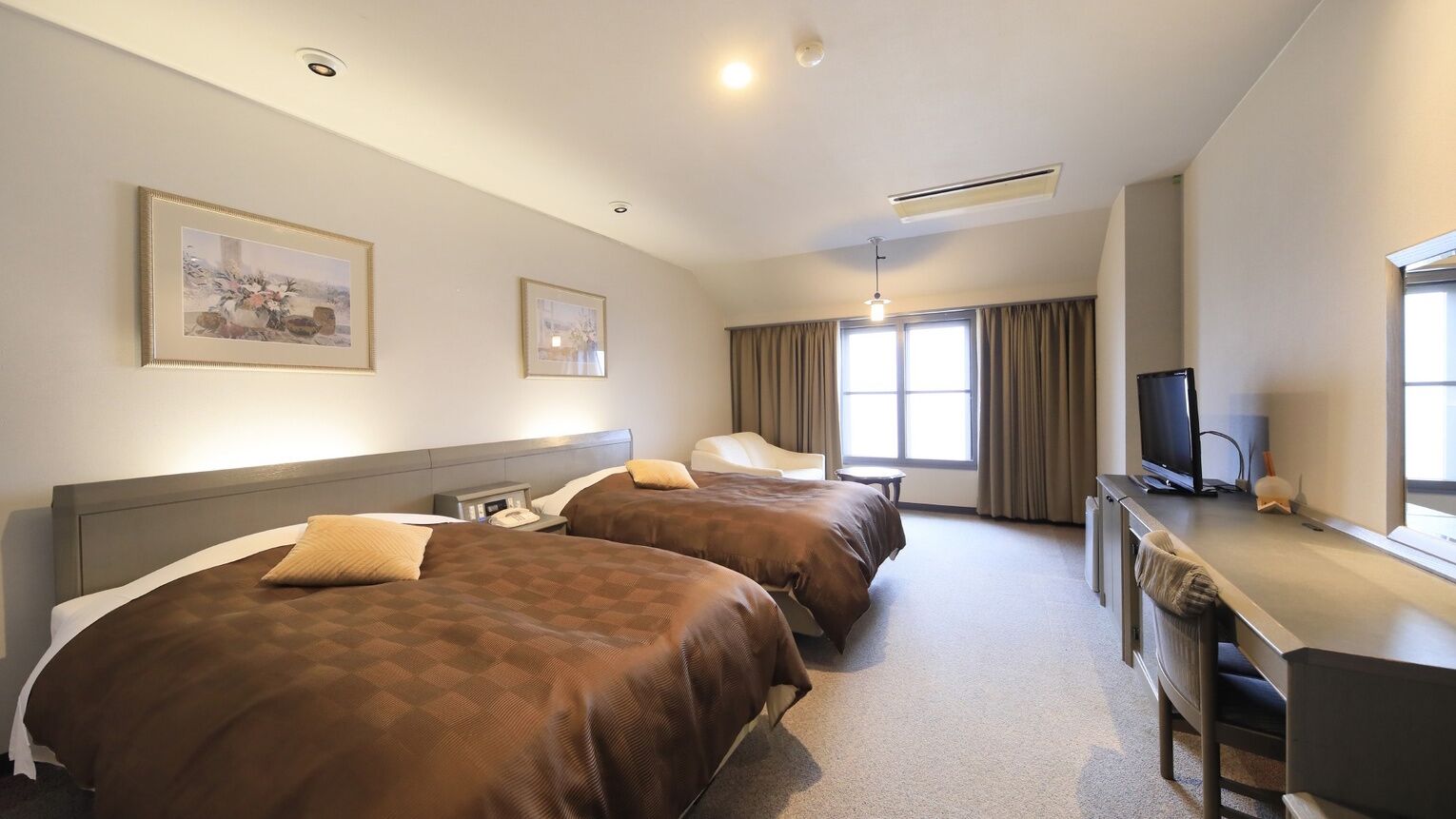 A hotel room with two beds, a desk, a television, and two framed pictures on the wall.