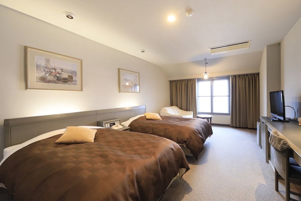 A hotel room with two beds, a desk, a television, and two framed pictures on the wall.