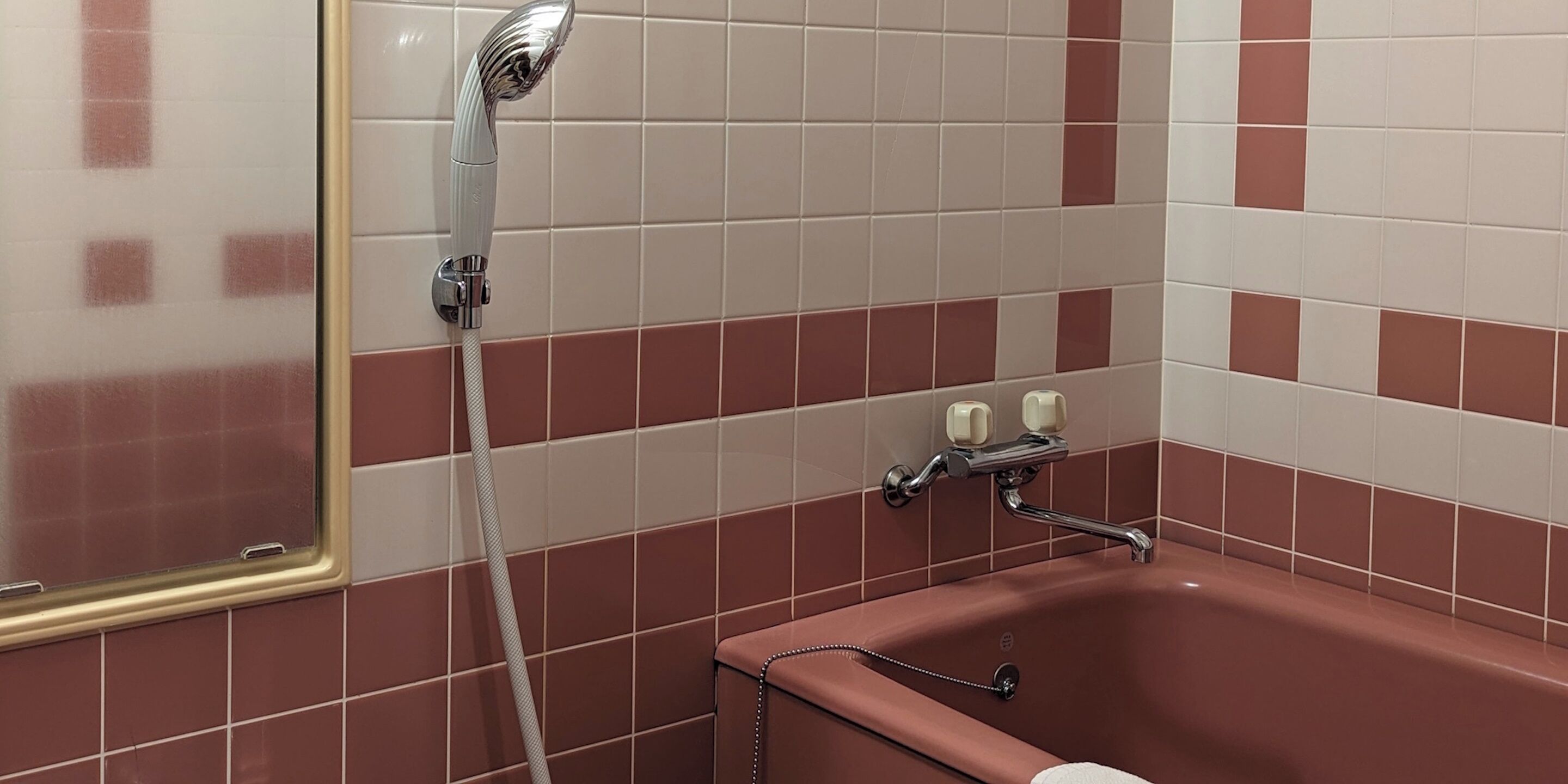 A bathroom with a bathtub, a shower head, and a window with a gold frame.