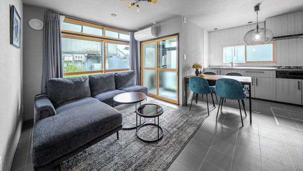 Un salon moderne avec un canapé gris, une petite table basse et un coin repas avec des chaises bleues.