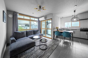 A modern living room with a grey sofa, a small coffee table, and a dining area with blue chairs. - AKATSUKI (Kamifurano)