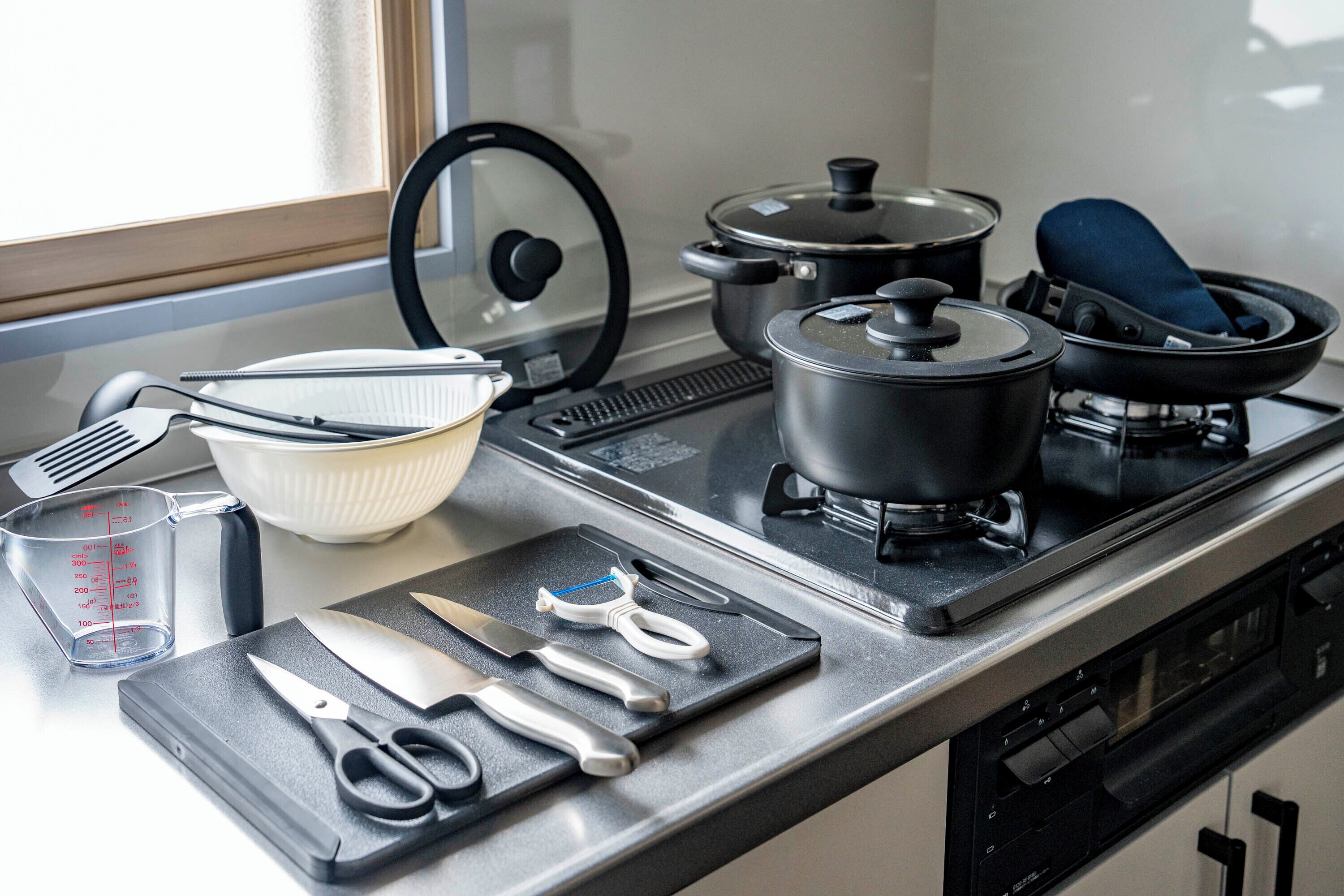 A kitchen with a stove, pots, a frying pan, a cutting board, a measuring cup, and various utensils.