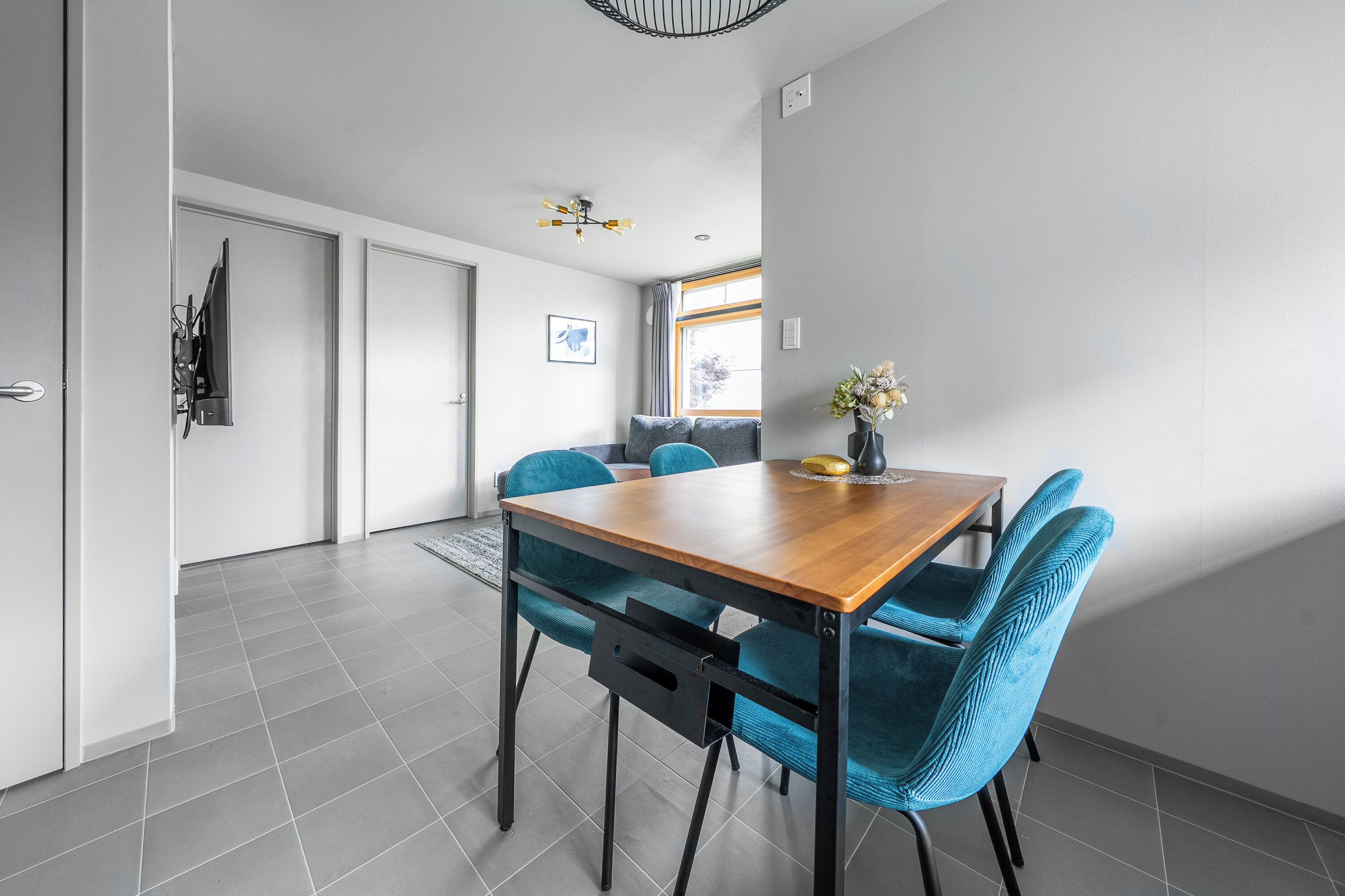 A modern dining area with a wooden table, blue upholstered chairs, and a small vase with flowers.