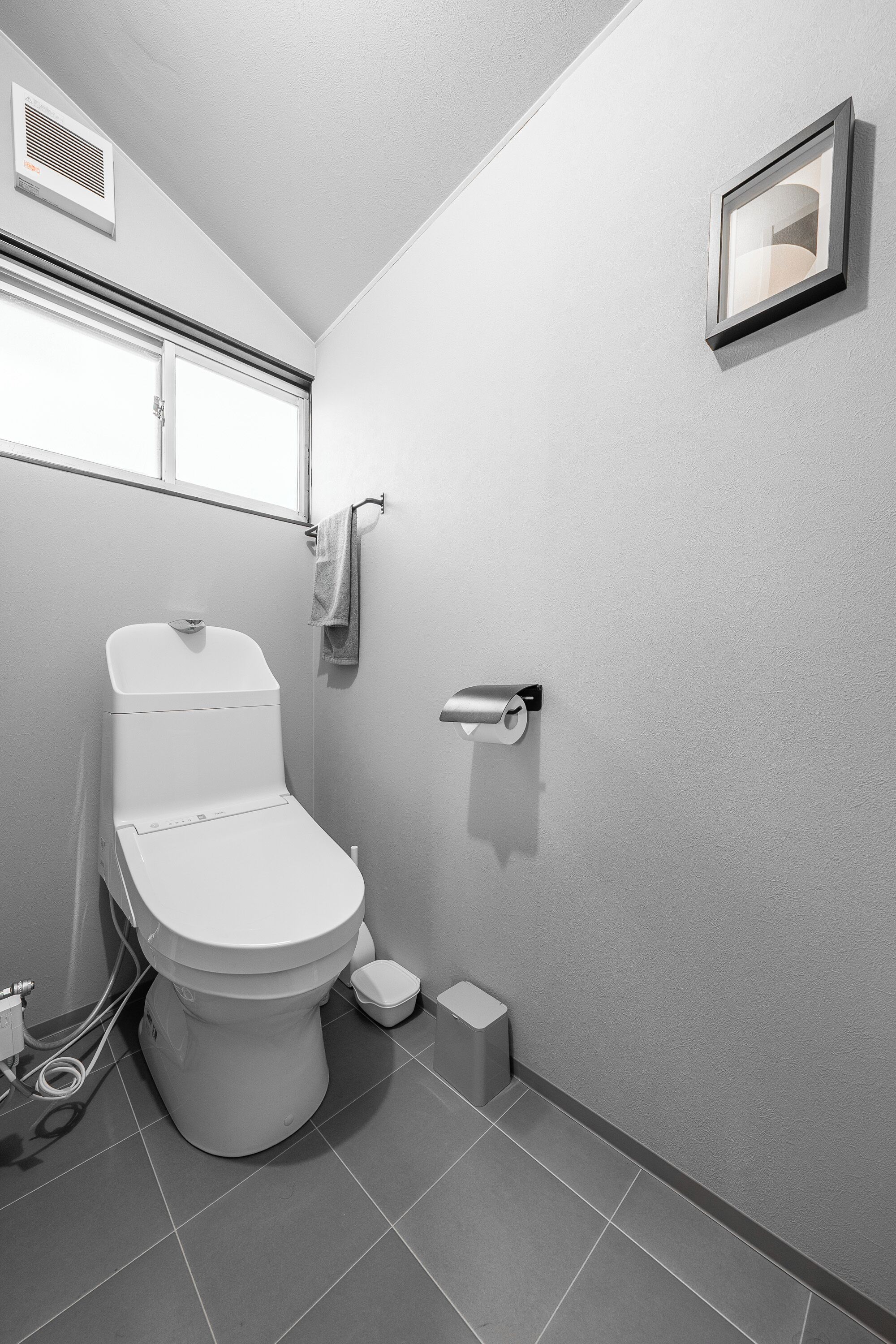 A modern bathroom with a toilet, a towel rack, a toilet paper holder, and a vent on the wall.