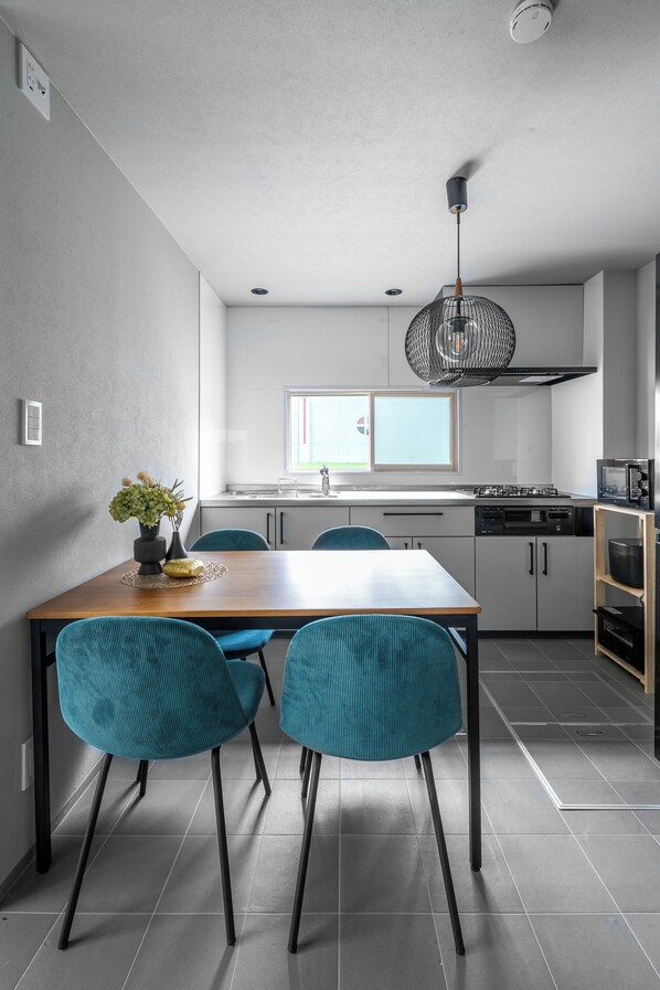 A modern kitchen with a dining area, featuring a wooden table, teal chairs, and a pendant light. - AKATSUKI (Kamifurano)