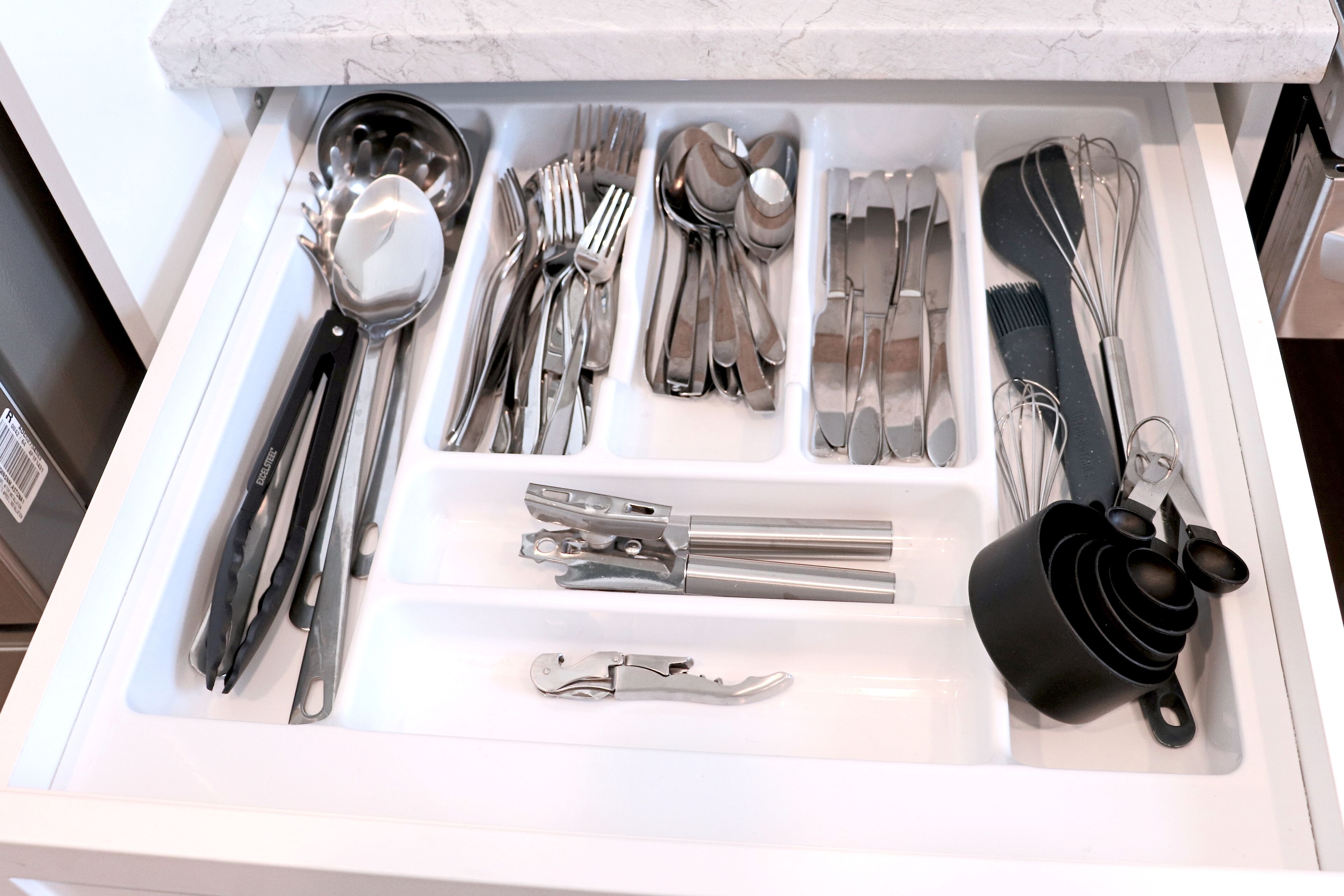 A drawer containing various kitchen utensils including spoons, forks, knives, and a grater.