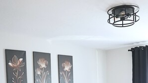 Una cama bien hecha con ropa blanca, una mesita de noche con lámpara y tres cuadros florales colgados en la pared.