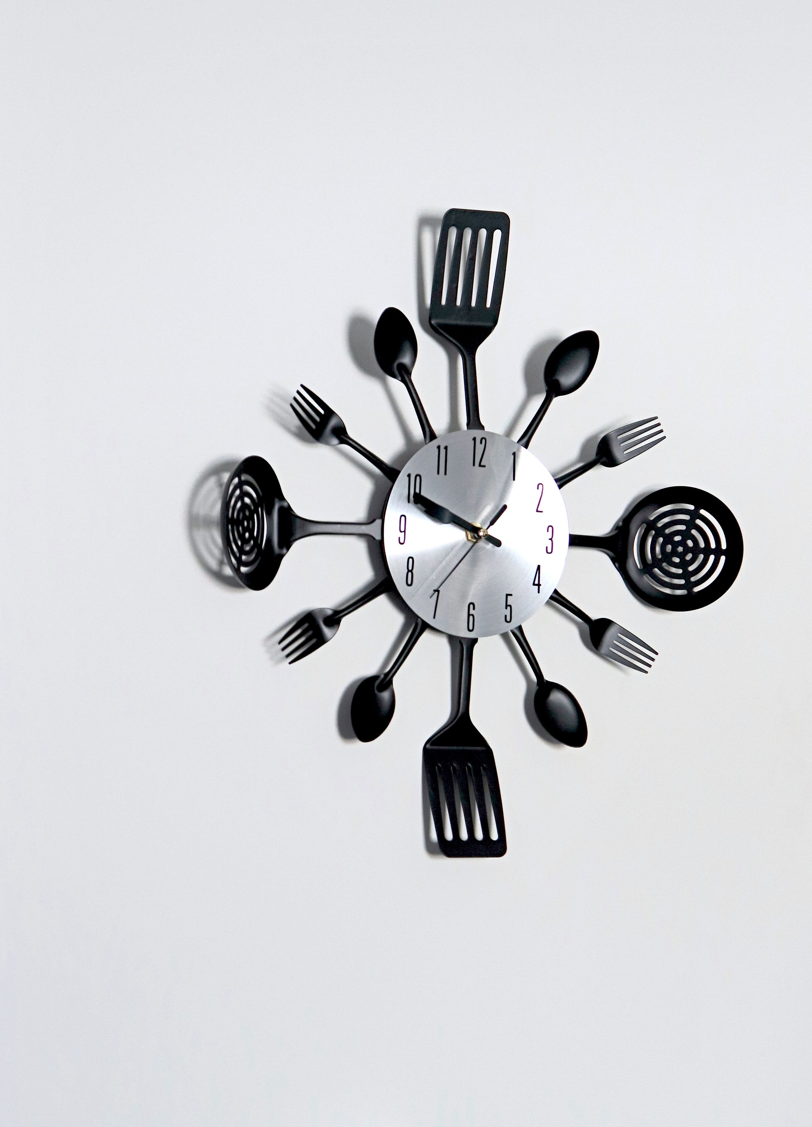 A wall clock with a unique design featuring kitchen utensils as hour markers.