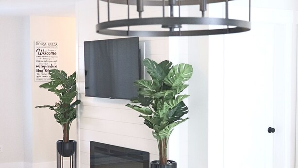 Un comedor moderno con una lámpara de araña de metal negro, una chimenea y dos plantas en macetas.