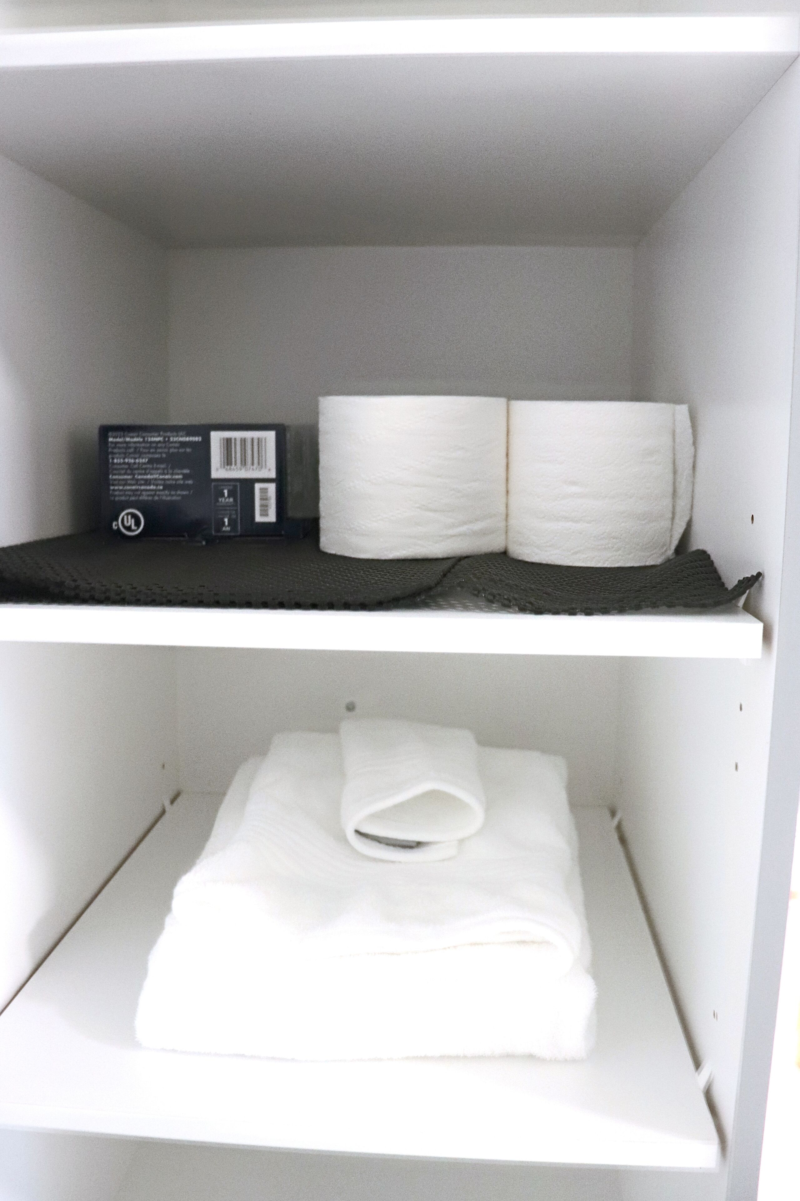 Ein weißes Regal mit einer Kiste und zwei Toilettenpapierrollen.